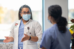 A healthcare professional wearing a mask speaks with a person in scrubs.